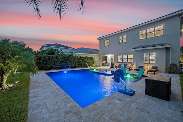 pool at dusk featuring pool water feature, a patio, and a hot tub