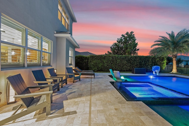 pool at dusk featuring a patio area and an in ground hot tub