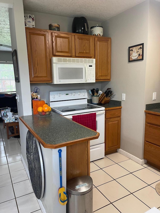 kitchen with kitchen peninsula, a textured ceiling, light tile patterned flooring, and white appliances