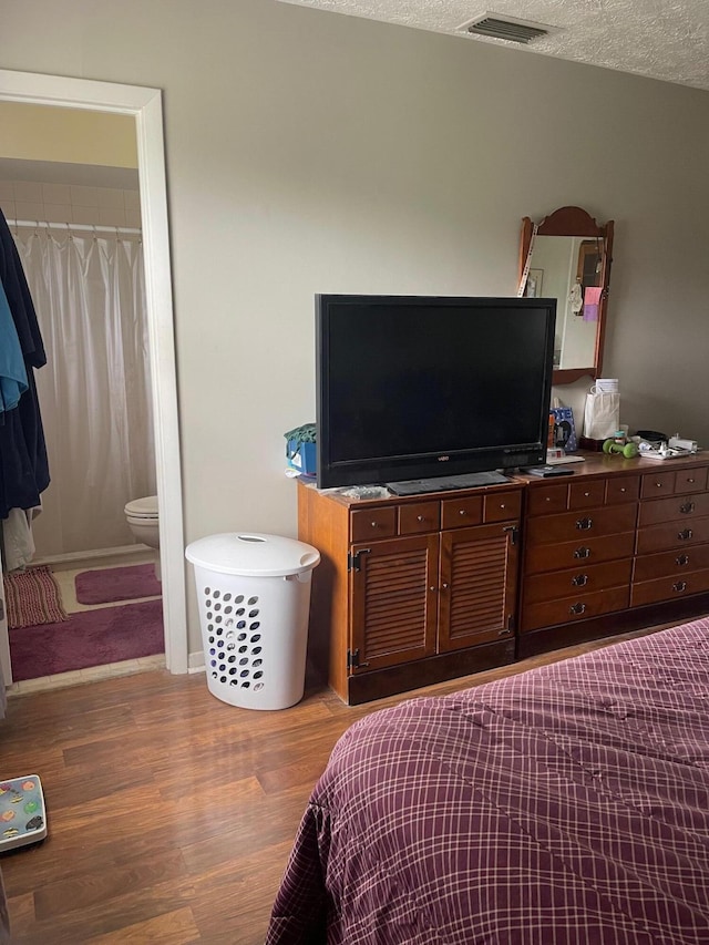 bedroom featuring hardwood / wood-style floors, a textured ceiling, and ensuite bath