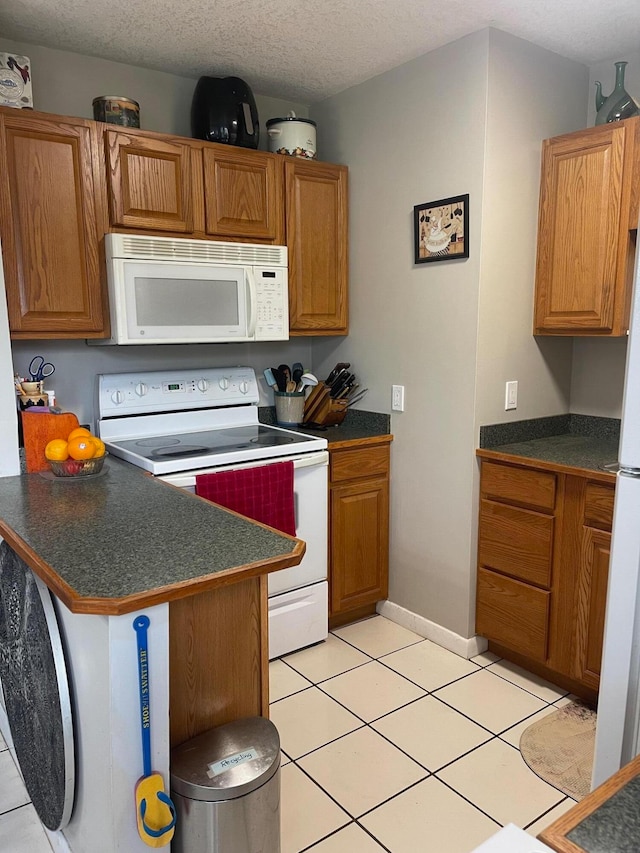 kitchen featuring light tile patterned flooring, kitchen peninsula, a textured ceiling, and white appliances