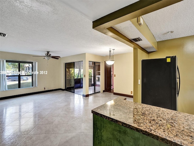 kitchen featuring ceiling fan, dark stone counters, pendant lighting, black fridge, and light tile patterned flooring