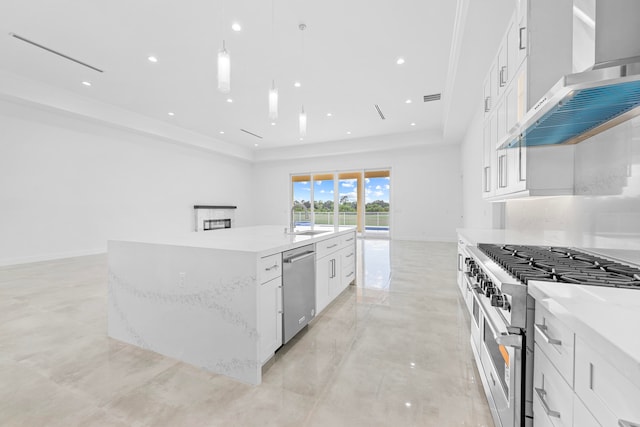 kitchen featuring appliances with stainless steel finishes, wall chimney exhaust hood, an island with sink, a tray ceiling, and white cabinetry