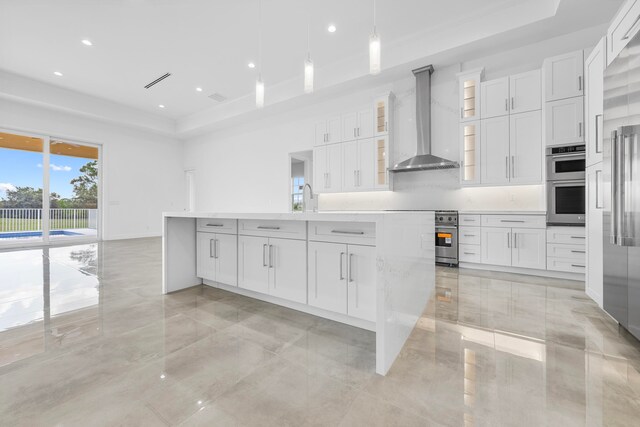 kitchen with a raised ceiling, wall chimney exhaust hood, white cabinetry, light tile patterned flooring, and stainless steel appliances