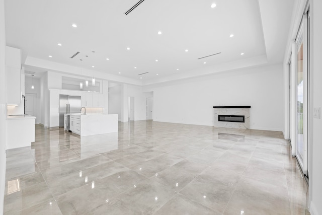 unfurnished living room featuring light tile patterned flooring, a high end fireplace, a raised ceiling, and sink