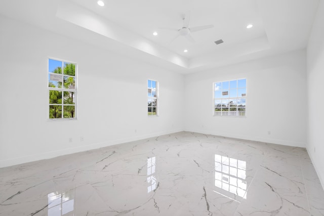 tiled empty room with ceiling fan, a wealth of natural light, and a tray ceiling