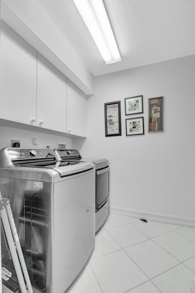 clothes washing area with light tile patterned floors, washing machine and dryer, a textured ceiling, and cabinets