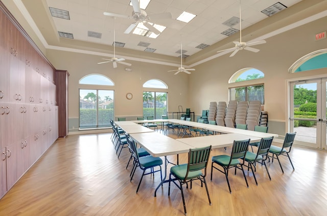 dining space with ceiling fan, light wood-type flooring, a raised ceiling, and a high ceiling