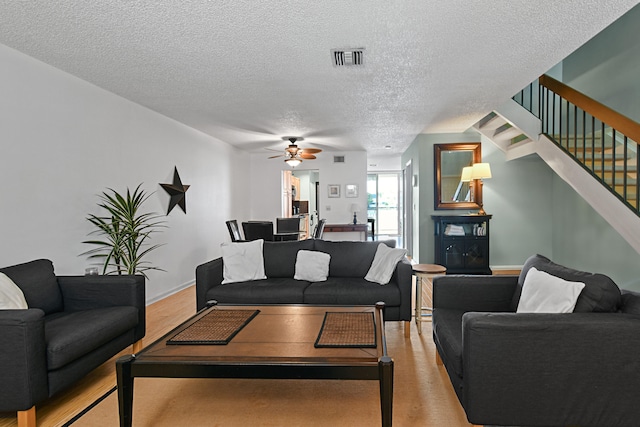 living room with light wood-type flooring, ceiling fan, and a textured ceiling