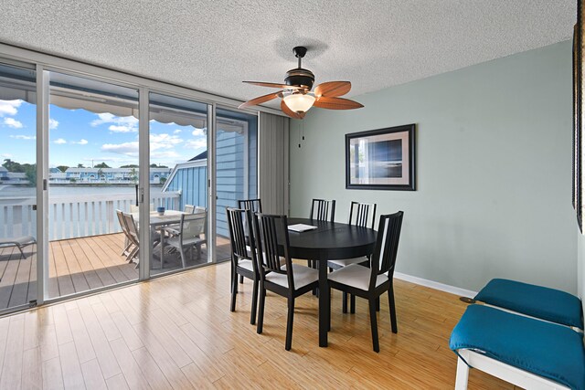 dining space featuring expansive windows, light hardwood / wood-style floors, a textured ceiling, a water view, and ceiling fan