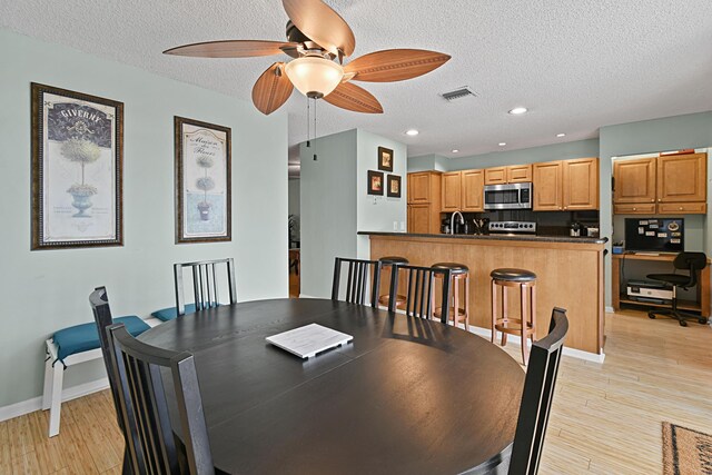 dining room featuring ceiling fan, a textured ceiling, light hardwood / wood-style flooring, and sink