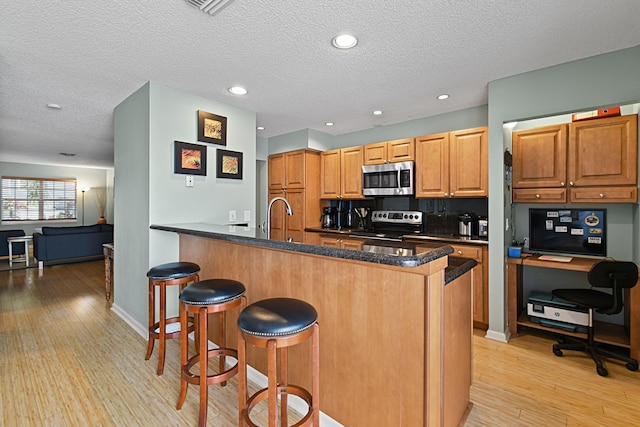 kitchen with a sink, tasteful backsplash, a kitchen bar, light wood-type flooring, and stainless steel appliances