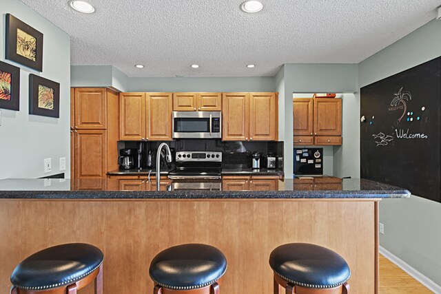 kitchen with a kitchen breakfast bar, dark stone countertops, appliances with stainless steel finishes, light hardwood / wood-style flooring, and a textured ceiling