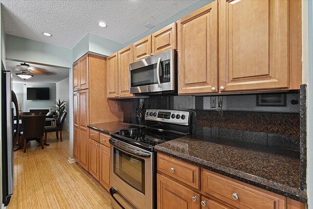 kitchen featuring ceiling fan, dark stone counters, light hardwood / wood-style flooring, tasteful backsplash, and appliances with stainless steel finishes