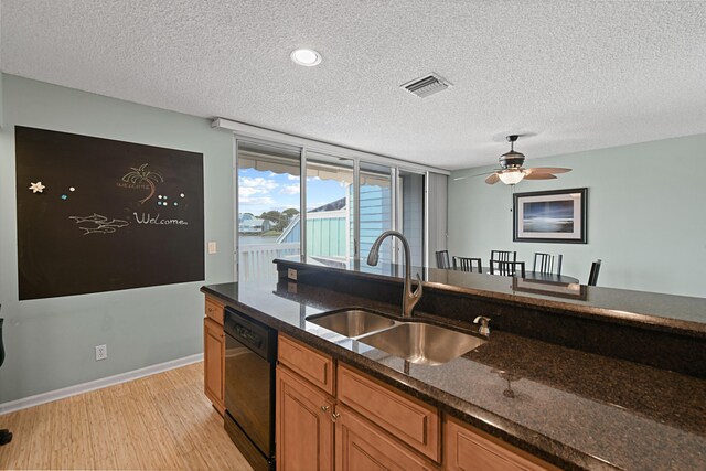 kitchen with black dishwasher, sink, dark stone countertops, light hardwood / wood-style flooring, and ceiling fan