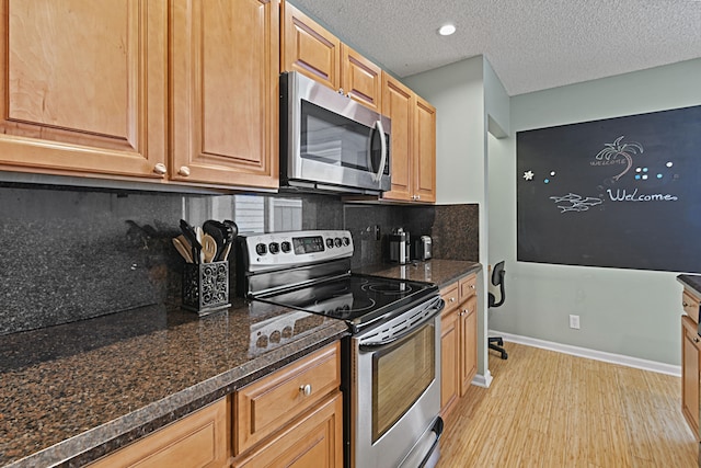 kitchen with backsplash, dark stone countertops, appliances with stainless steel finishes, light hardwood / wood-style flooring, and a textured ceiling