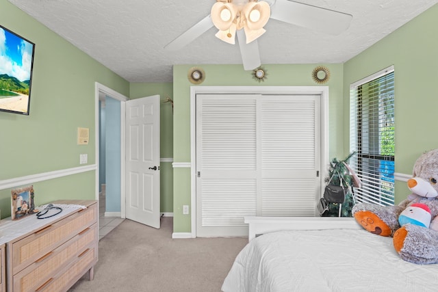 bedroom featuring a closet, light colored carpet, a ceiling fan, and a textured ceiling