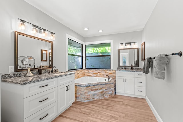 full bath featuring a bath, a sink, wood finished floors, and two vanities