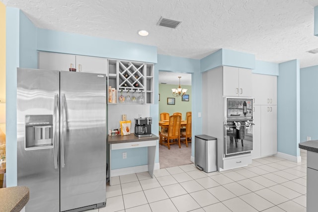 kitchen featuring visible vents, white cabinetry, stainless steel fridge, an inviting chandelier, and light tile patterned floors