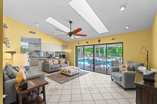 living area featuring visible vents, ceiling fan, lofted ceiling with skylight, light tile patterned floors, and a textured ceiling