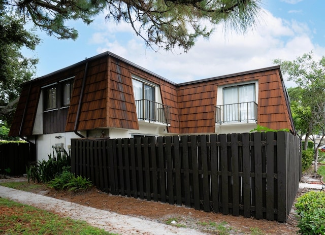 view of home's exterior featuring fence and mansard roof