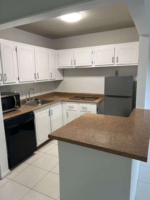 kitchen with light tile patterned floors, white cabinets, sink, and black appliances