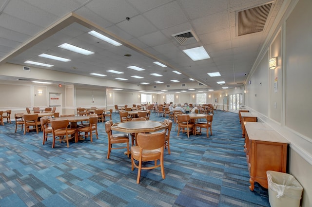 carpeted dining space with a drop ceiling