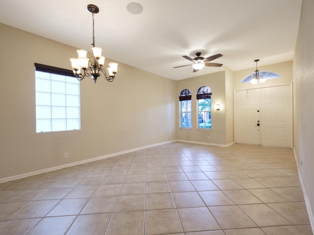 tiled spare room featuring ceiling fan with notable chandelier and a wealth of natural light