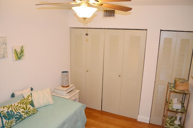 bedroom with light hardwood / wood-style floors, multiple closets, and ceiling fan