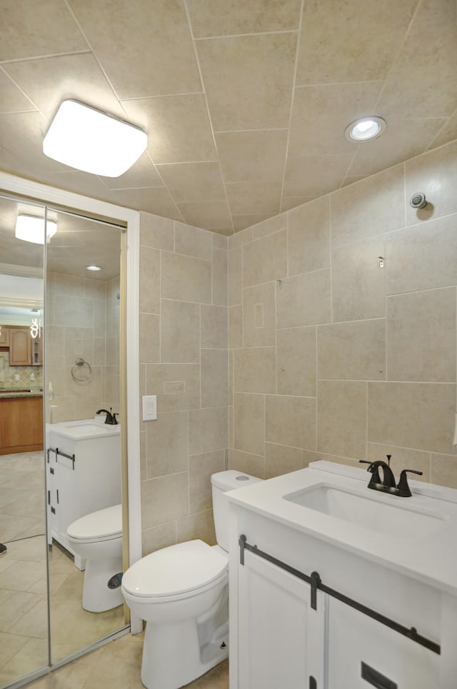 bathroom featuring vanity, tasteful backsplash, tile patterned floors, tile walls, and toilet