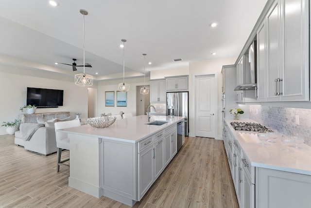 kitchen with a kitchen island with sink, tasteful backsplash, stainless steel appliances, sink, and light hardwood / wood-style floors