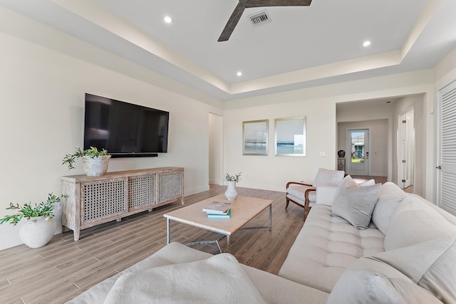 living room with light wood-type flooring, a tray ceiling, and ceiling fan