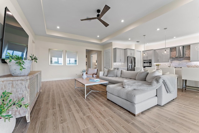 living room with a tray ceiling, ceiling fan, and light hardwood / wood-style floors