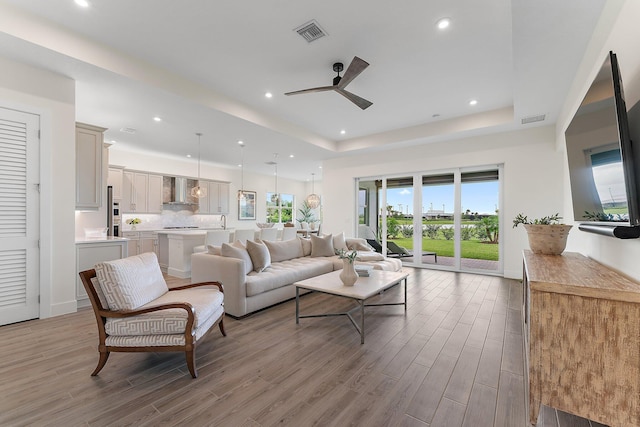 living room with light wood-type flooring, plenty of natural light, a tray ceiling, and ceiling fan