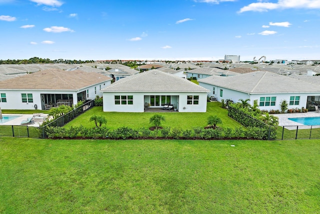 rear view of property featuring a fenced in pool, a patio area, and a lawn