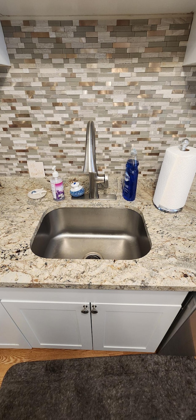 interior details featuring sink, light stone counters, and decorative backsplash