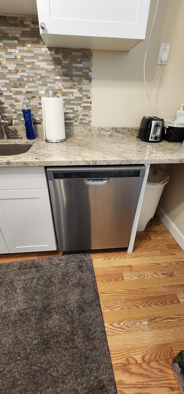 interior details with light wood-type flooring, stainless steel dishwasher, backsplash, white cabinetry, and light stone counters