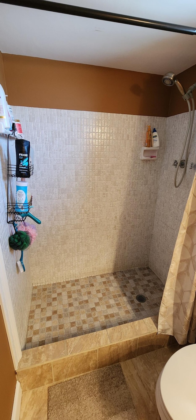 bathroom with tiled shower, toilet, and tile patterned flooring