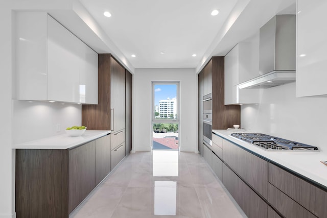 kitchen with wall chimney exhaust hood, dark brown cabinets, stainless steel gas stovetop, and light tile patterned floors