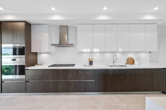 kitchen featuring sink, light tile patterned floors, wall chimney exhaust hood, white cabinetry, and stainless steel appliances