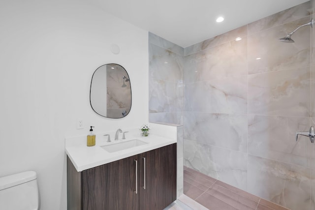 bathroom featuring toilet, a tile shower, and vanity