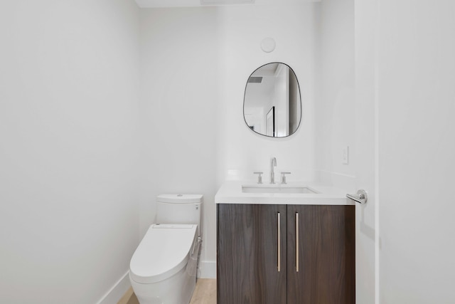 half bath with baseboards, vanity, and toilet