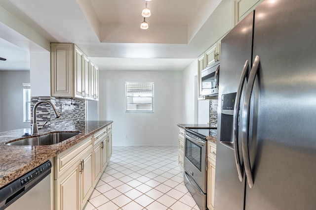 kitchen with backsplash, sink, appliances with stainless steel finishes, cream cabinets, and a raised ceiling