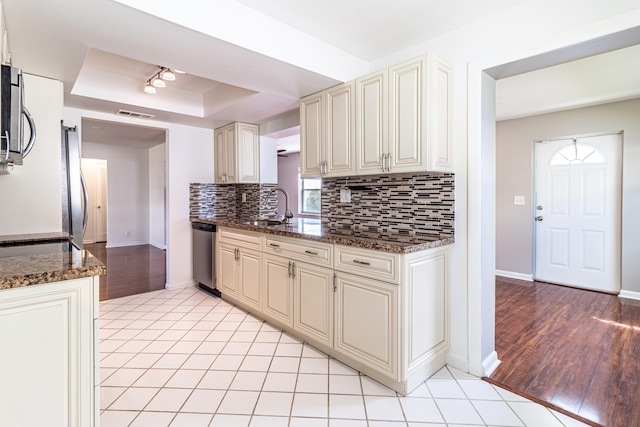 kitchen featuring dark stone countertops, light hardwood / wood-style flooring, a tray ceiling, and appliances with stainless steel finishes