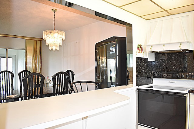 kitchen featuring a notable chandelier, custom range hood, black refrigerator, white electric stove, and decorative backsplash