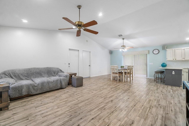 living area featuring visible vents, a ceiling fan, vaulted ceiling, light wood-type flooring, and baseboards