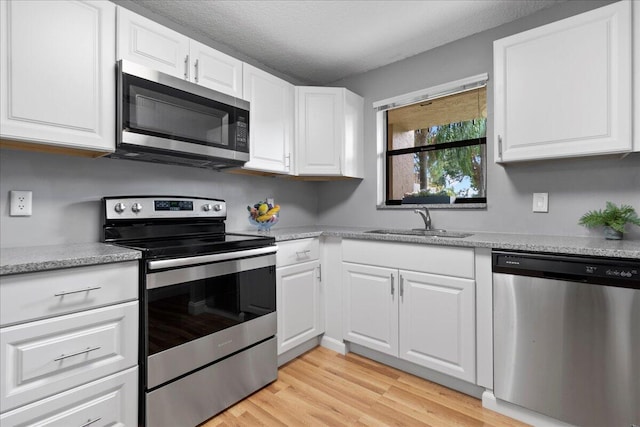 kitchen featuring white cabinets, appliances with stainless steel finishes, light wood-type flooring, and sink