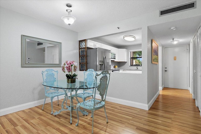 dining room with a textured ceiling, light hardwood / wood-style flooring, and sink