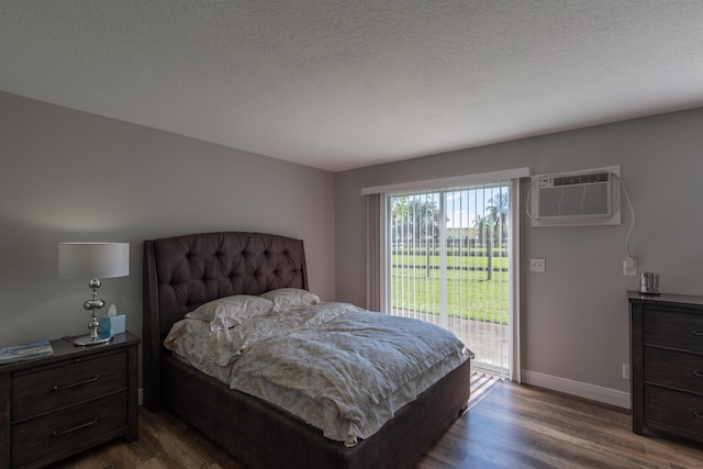 bedroom with an AC wall unit, access to outside, a textured ceiling, and hardwood / wood-style floors