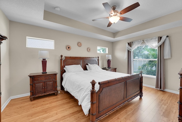 bedroom featuring light wood-type flooring, ceiling fan, and a tray ceiling